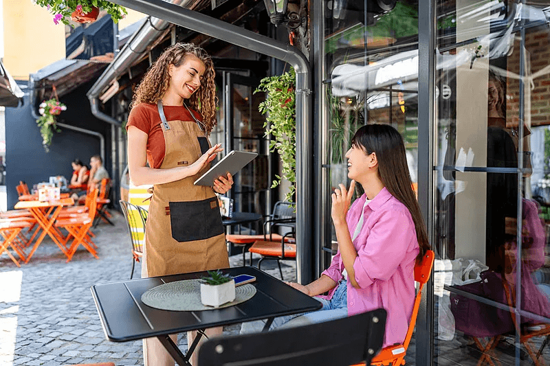 A cafe team member serving a guest seated on the terrace